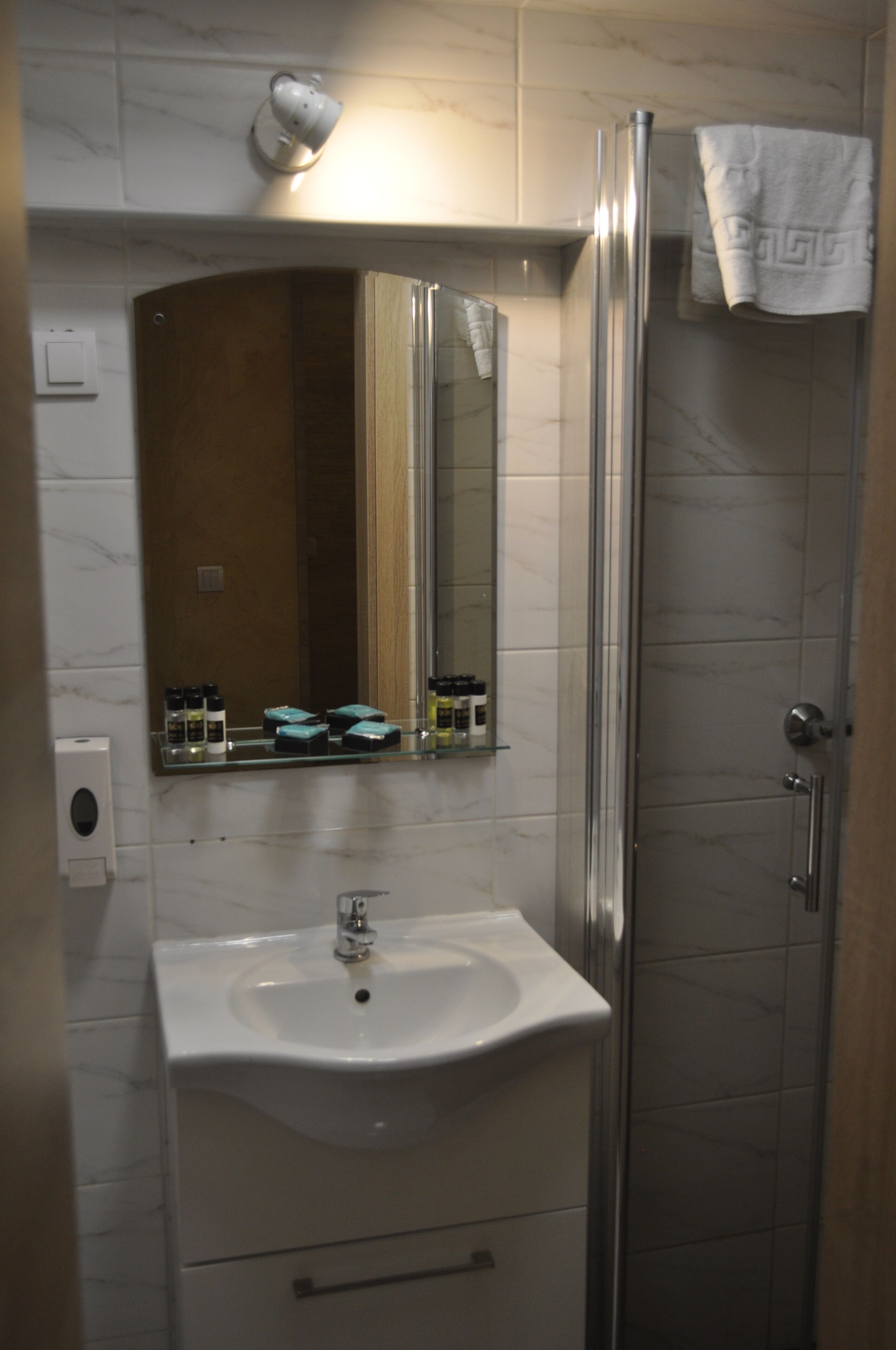 A bathroom with a white sink, a mirror, a glass shower enclosure, and a towel hanging on the wall.
