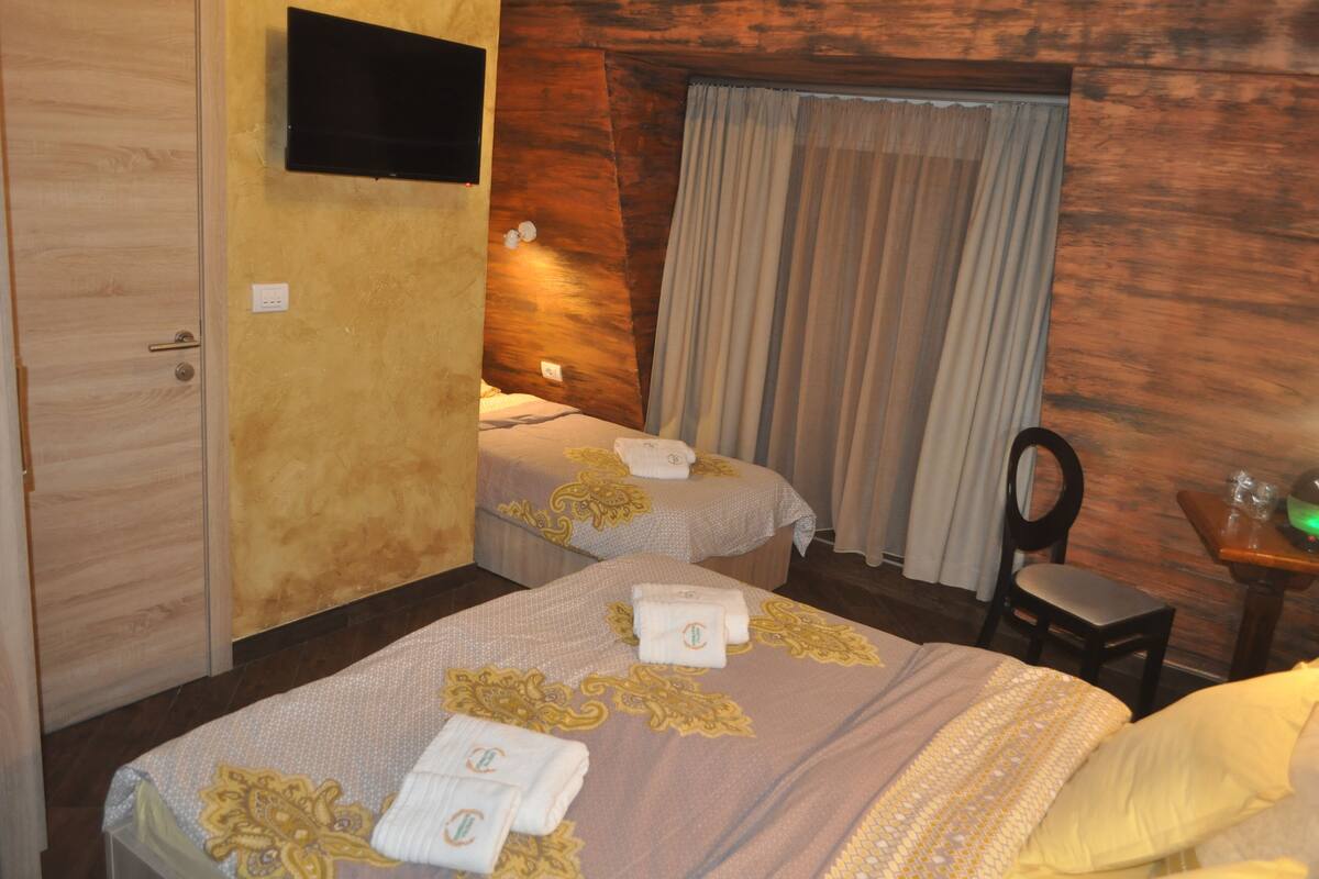 A hotel room with two beds, a TV mounted on the wall, a wooden door, and a chair.