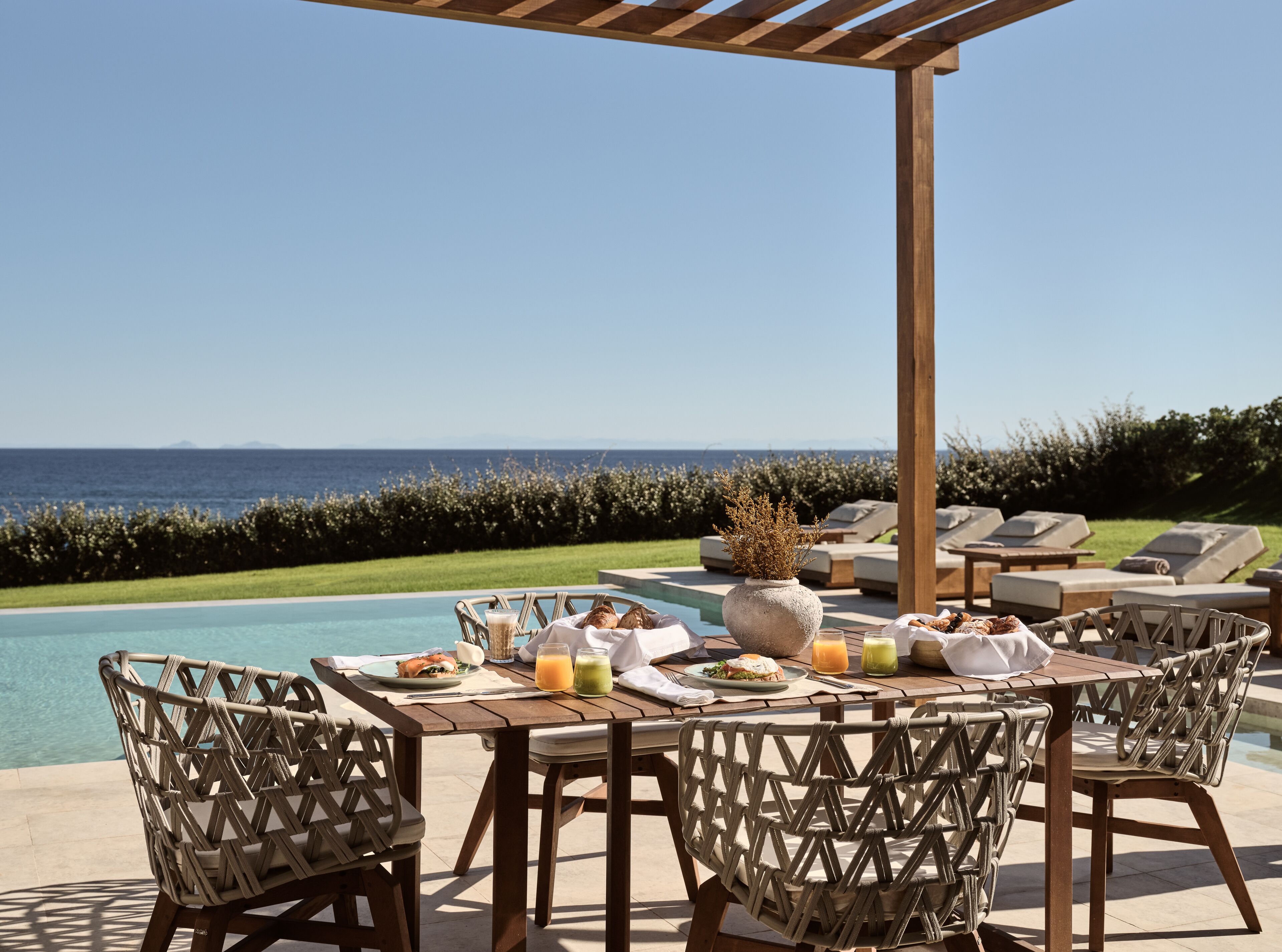 Un espace extérieur aménagé pour les repas, avec vue sur l’océan, une piscine et des chaises longues.