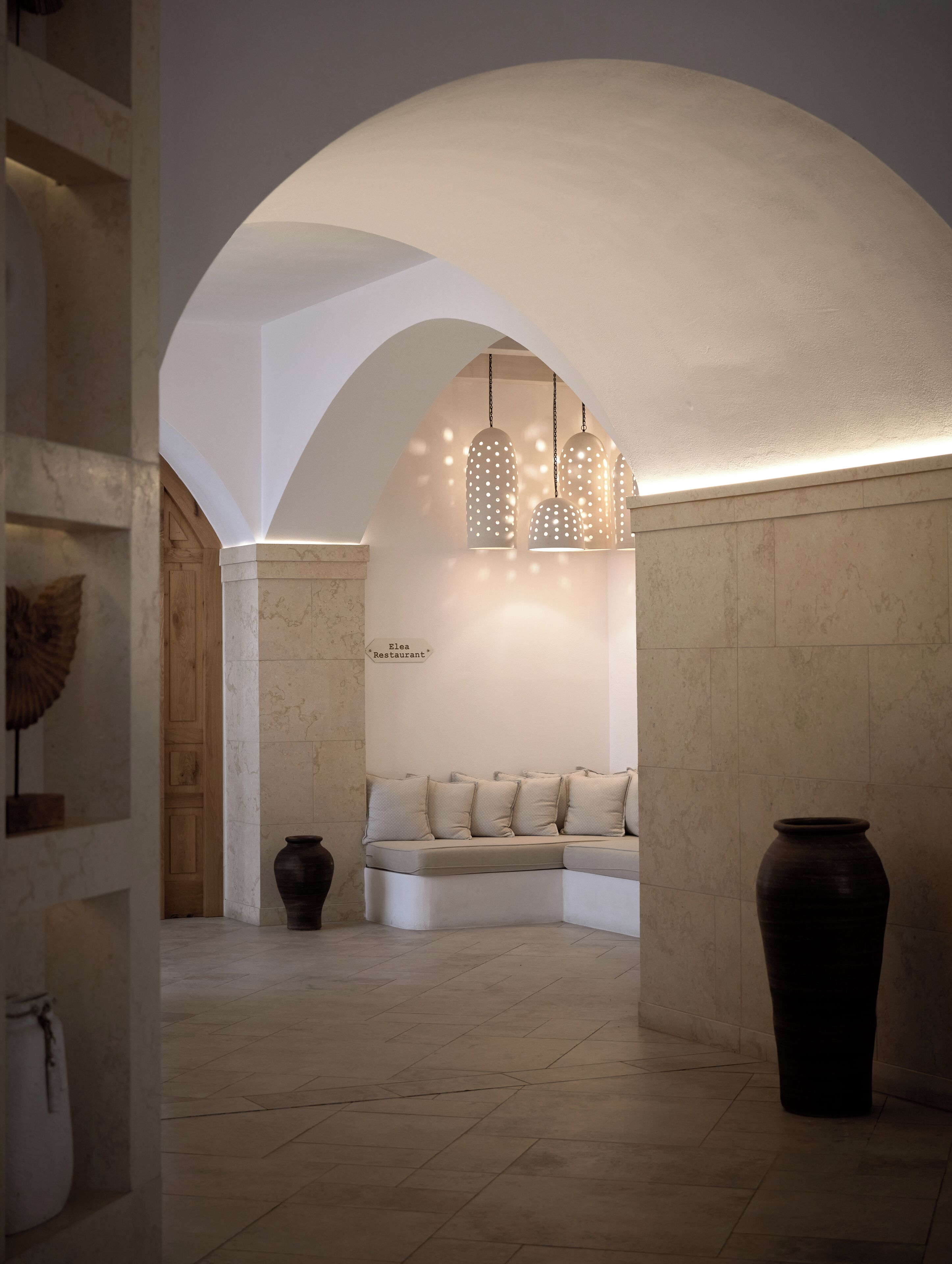 A modern interior with a seating area under a white archway, a hanging light fixture, and a large vase.