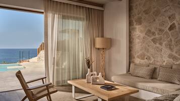 A room with a view of the sea, a wooden table, a sofa, and a lamp.