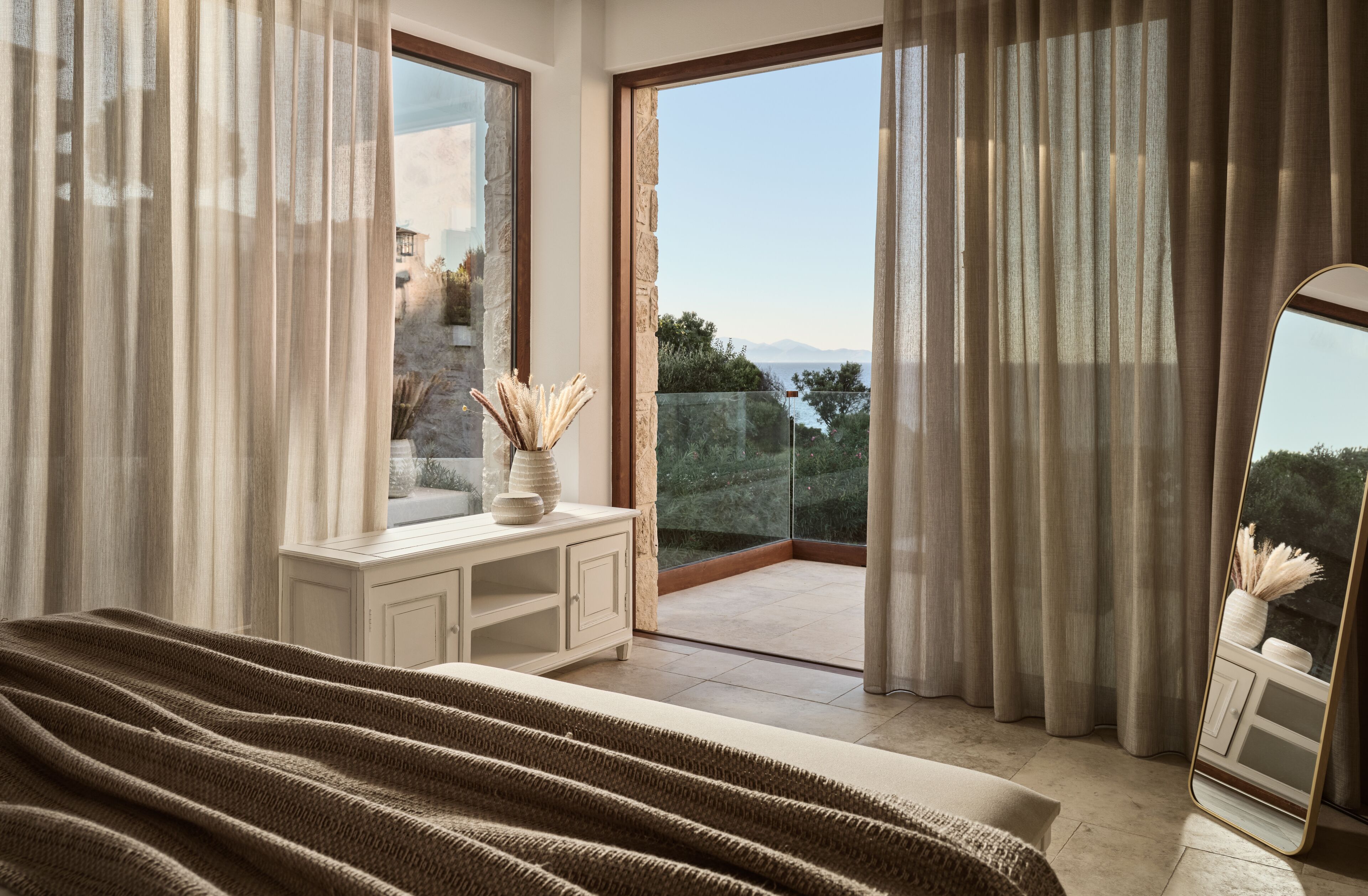 A bedroom with a large bed, a dresser, and a view of the outdoors through a sliding glass door.