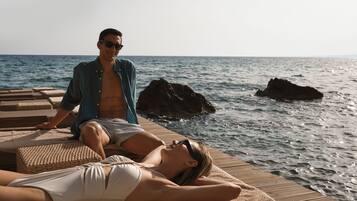 A couple relaxing on a wooden deck with a view of the sea and rocks.