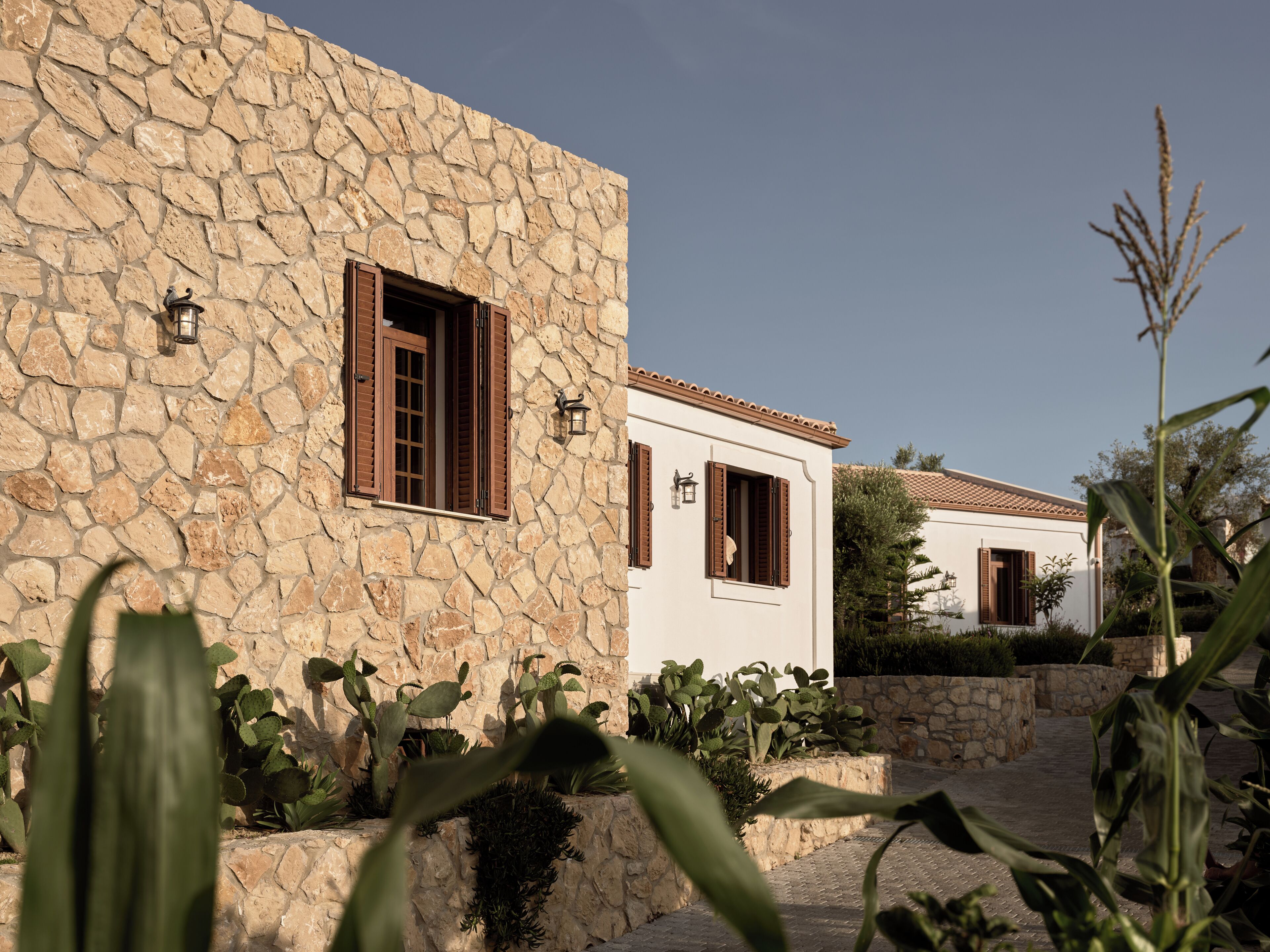 A stone building with wooden shutters and a white building in the background.