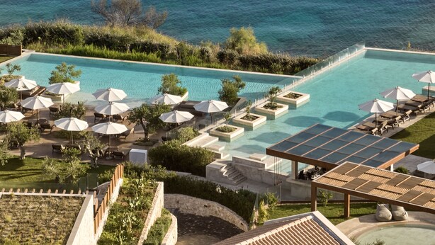 A large outdoor swimming pool with multiple sun loungers and umbrellas, surrounded by greenery and overlooking a body of water. - Lesante Cape - The Leading Hotels of the World (Zakynthos)