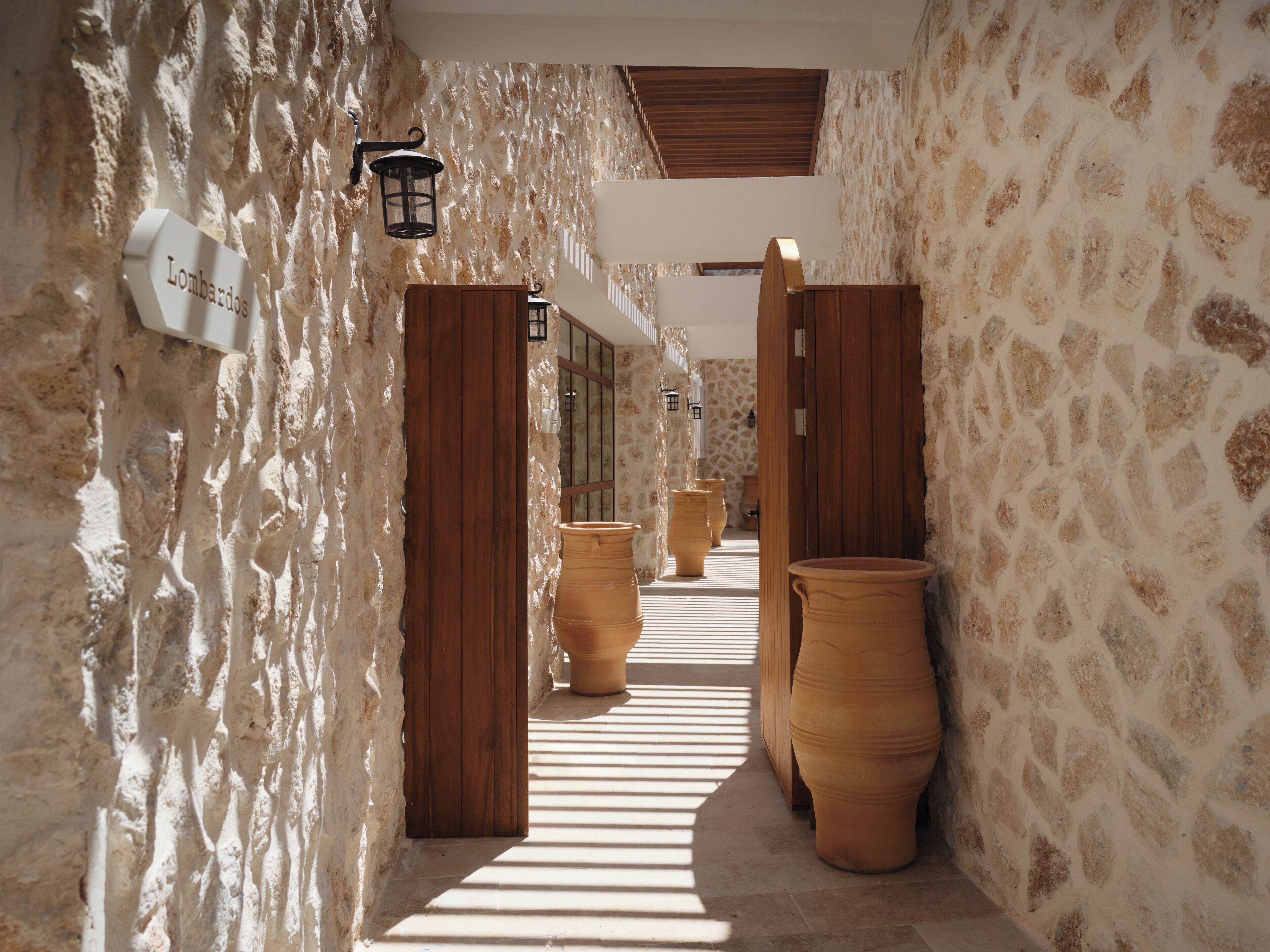 A corridor with stone walls, wooden doors, and terracotta pots.