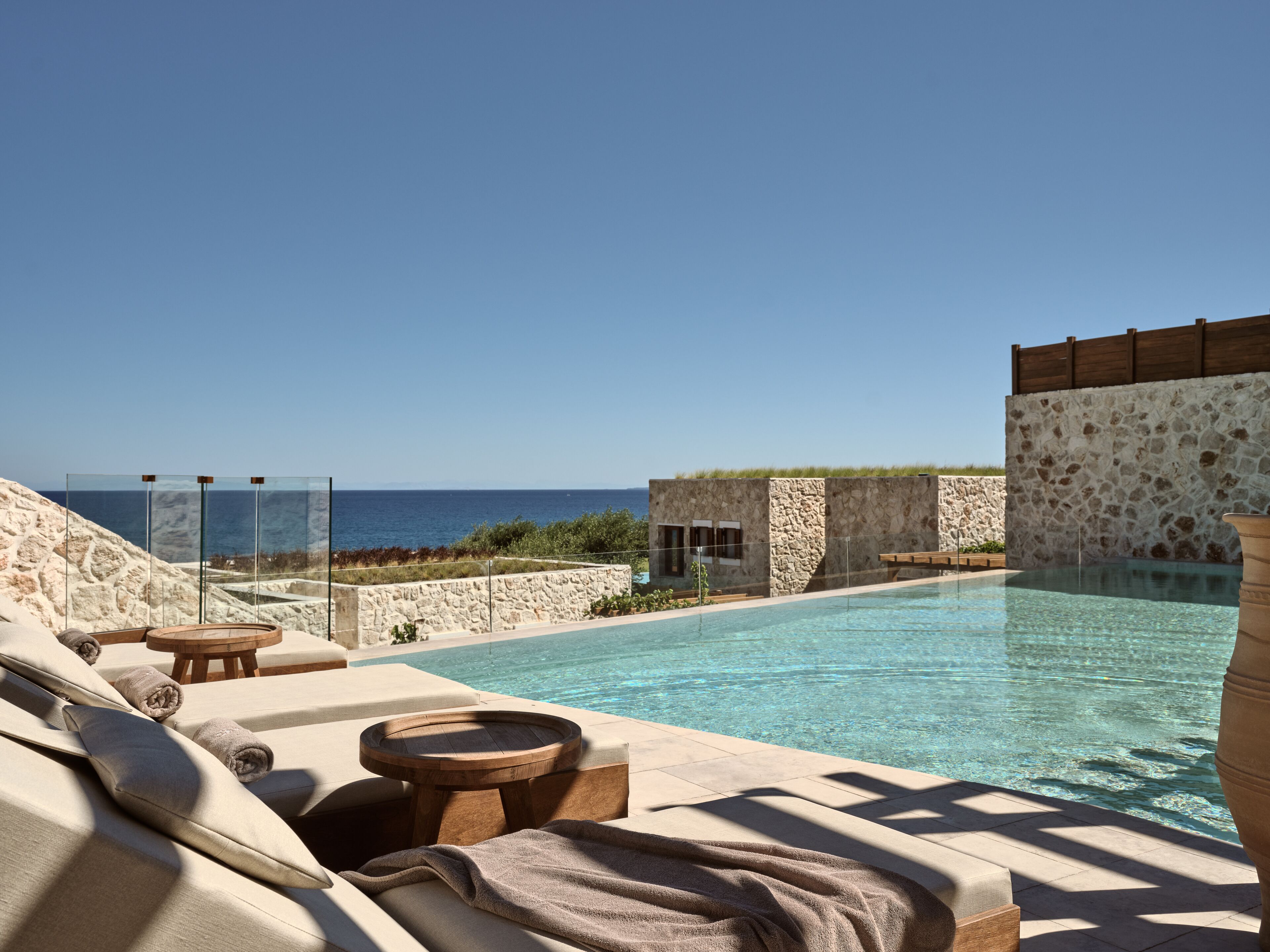 Ein Poolbereich mit Liegestühlen und einer Steinmauer, mit Blick auf das klare, blaue Meer.