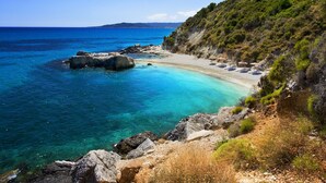 A coastal beach with clear turquoise waters, rocky shoreline, and a hilly backdrop. - Lesante Cape - The Leading Hotels of the World (Zakynthos)