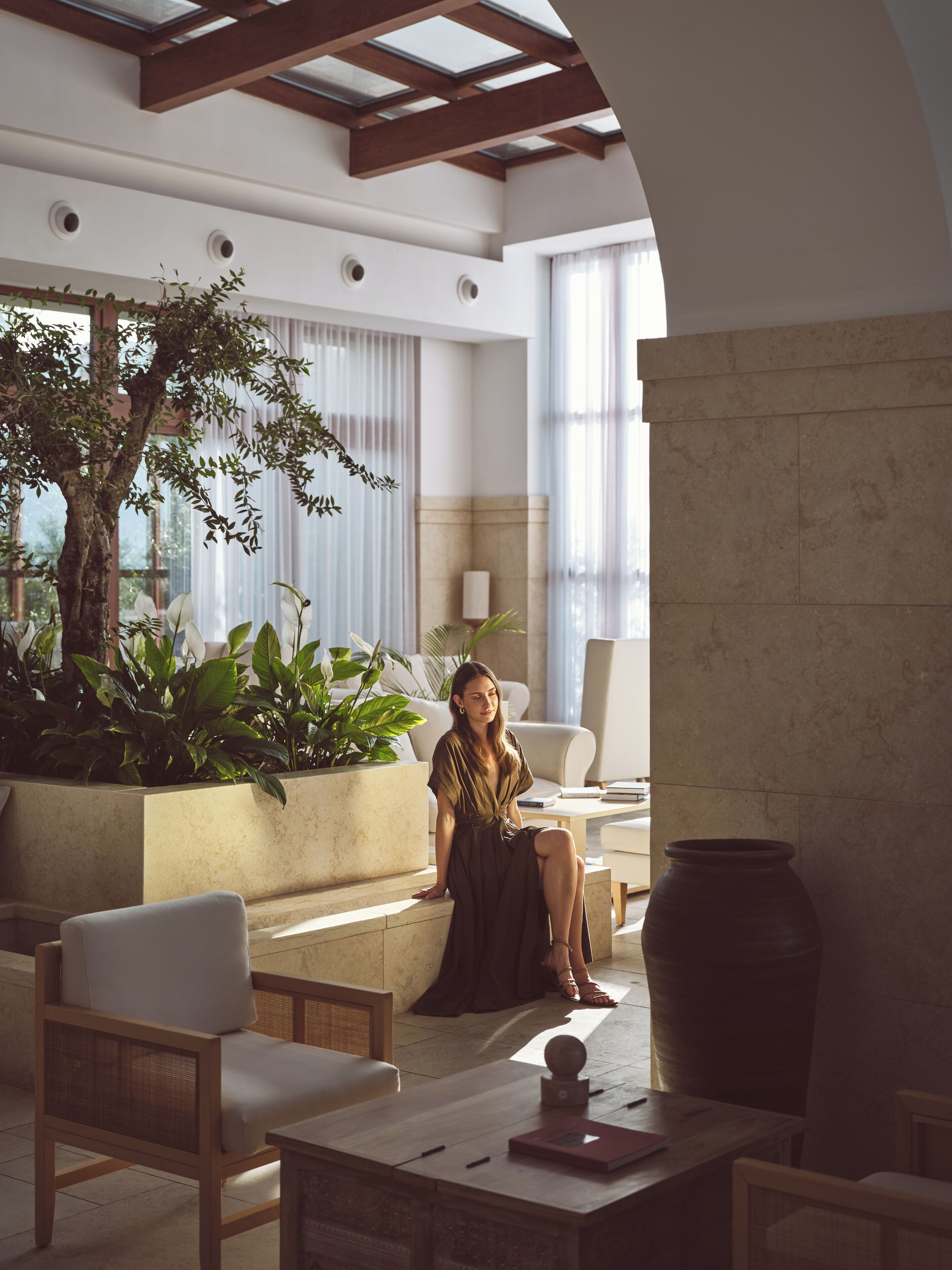 A spacious indoor area with a large plant, a seating area with chairs, and a large vase on a table.