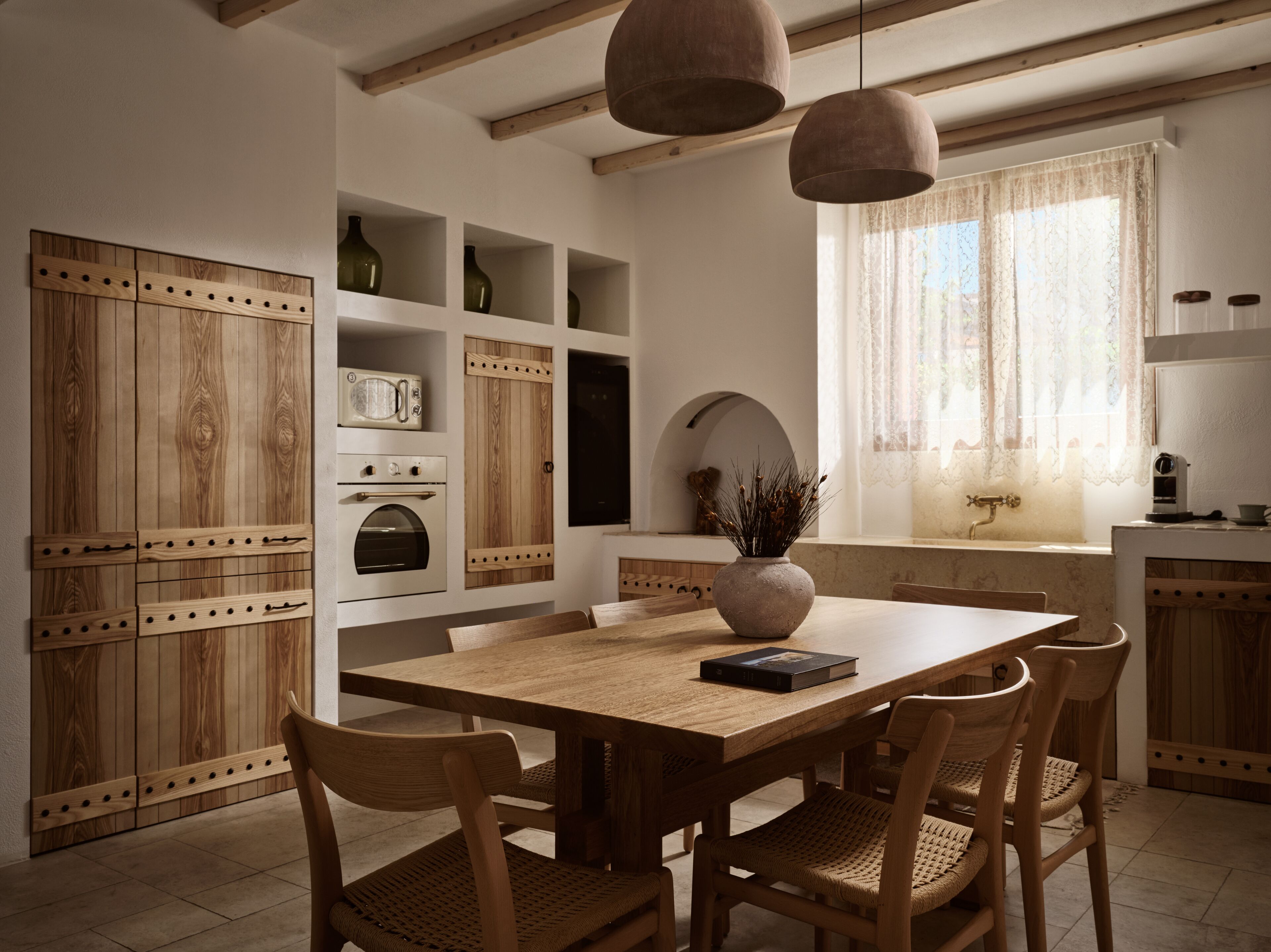 A wooden dining table with chairs, a vase with dried plants, and built-in wooden cabinets with shelves.