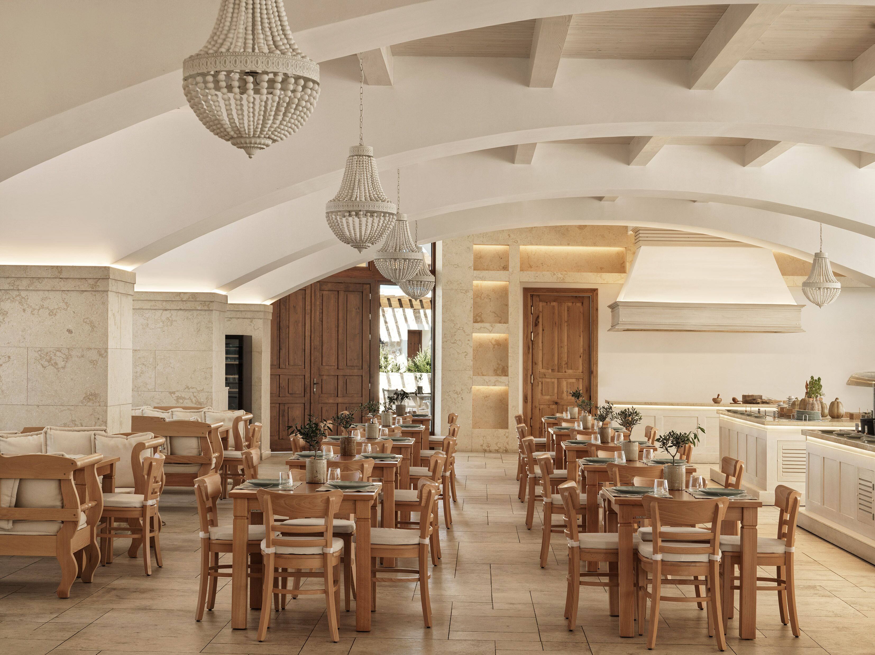 Un'ampia sala da pranzo con tavoli e sedie in legno, un angolo cottura e un soffitto alto con lampadari.