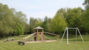 A playground with a wooden climbing structure, a swing set, and a picnic table. - Urlauberdorf 50a, Deutschland (Ostseebad Boltenhagen)