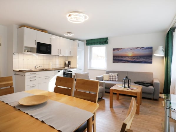 Une cuisine moderne avec des meubles blancs, un four à micro-ondes et un coin repas comprenant une table et des chaises en bois.