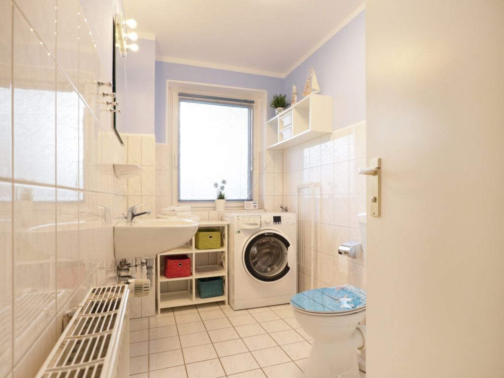 Un baño pequeño con lavadora, inodoro y ventana que proporciona luz natural.