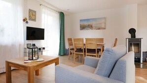 A living room with a sofa, wooden table, TV, and a fireplace. - Urlauberdorf 50a, Deutschland (Ostseebad Boltenhagen)