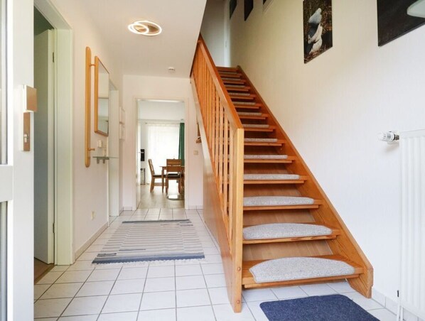 A staircase with wooden steps and cushioned handrails, leading to a room with a white radiator and a framed picture on the wall.