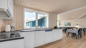 Een moderne keuken met een centraal eiland, een zithoek met tafel en stoelen, en een uitzicht door grote ramen.