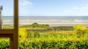 Uitzicht op de oceaan door een raam, met een strand en begroeiing op de voorgrond.