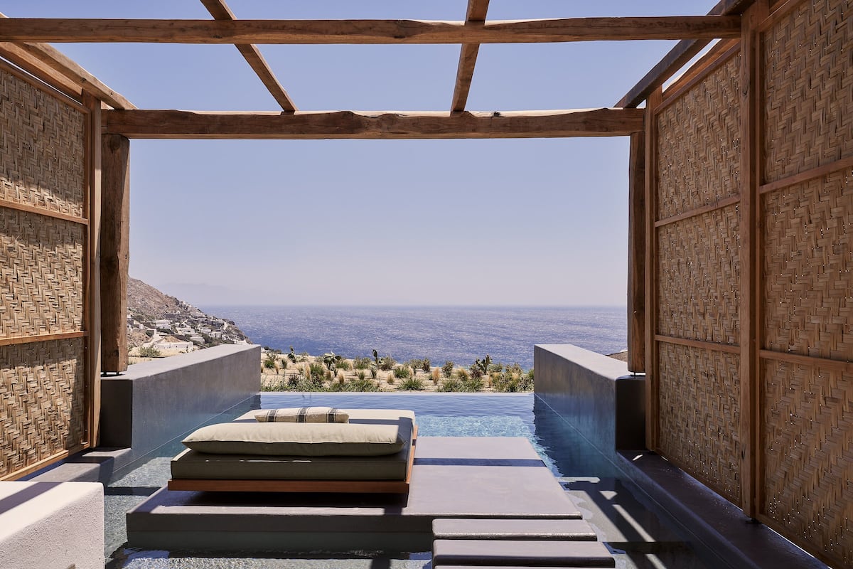 Piscina privativa infinita com vista para a costa, vigas de madeira e área de estar com assentos acolchoados.