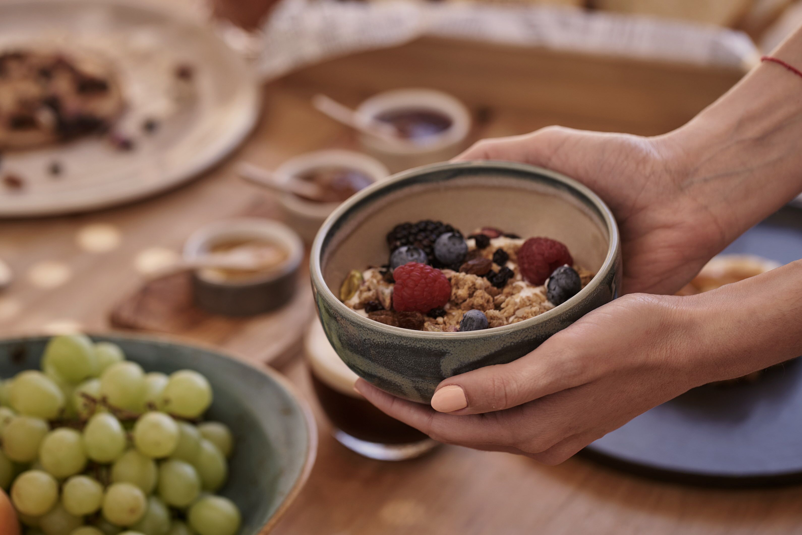 A bowl of cereal with berries and a bowl of grapes on a table.