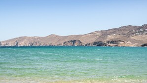 Una playa con agua turquesa cristalina, una orilla arenosa y colinas rocosas al fondo.