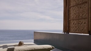 Una habitación con vista al océano, un sombrero de paja sobre un cojín y un panel de pared de madera.