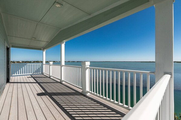 A covered wooden deck with white railings overlooking a calm body of water.