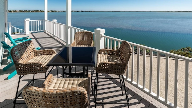 Terraza exterior cubierta con muebles de mimbre y una mesa, con vista a una masa de agua tranquila.