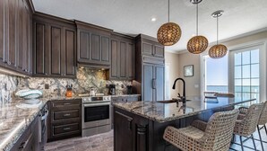 Una cocina moderna con armarios de madera oscura, encimera de granito, horno empotrado y una isla grande con taburetes de bar.