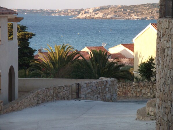 A coastal view with stone walls, a paved area, and buildings with red-tiled roofs.