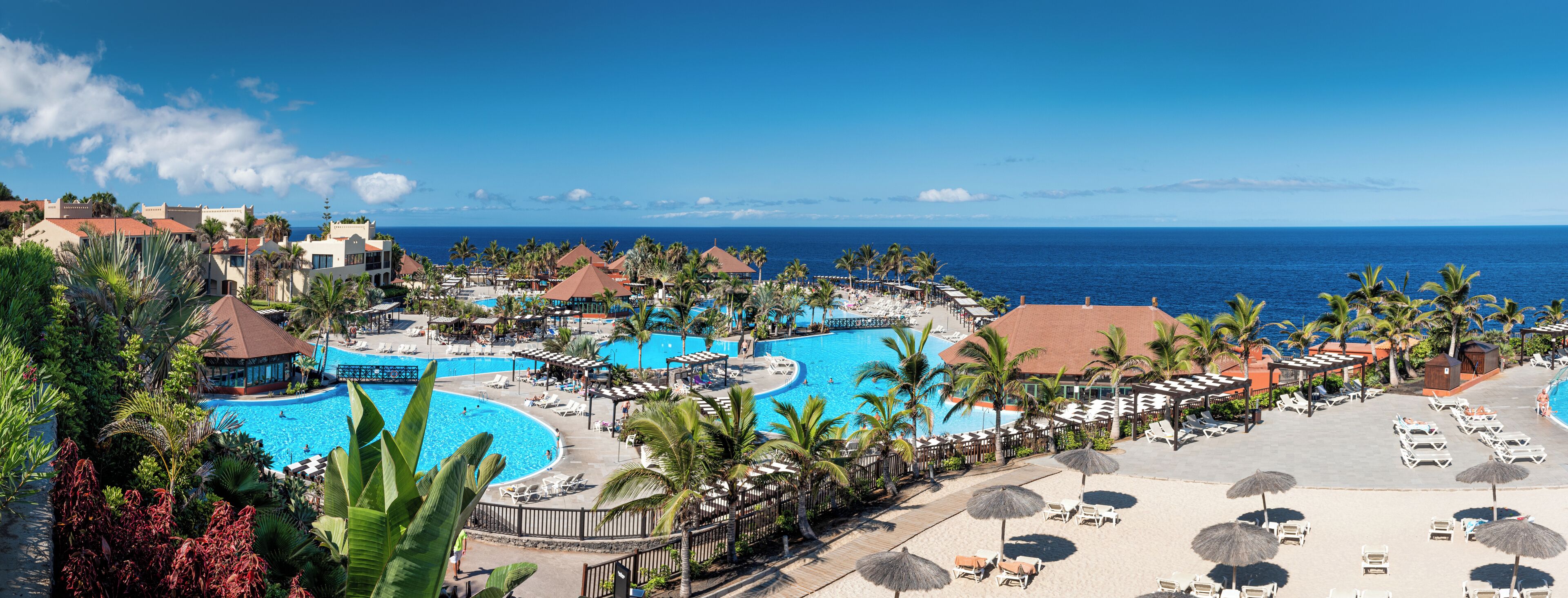 Un resort con varias piscinas, palmeras y vistas al océano.