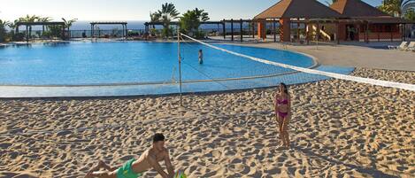 A beach volleyball court adjacent to a swimming pool with a clear view of the ocean.