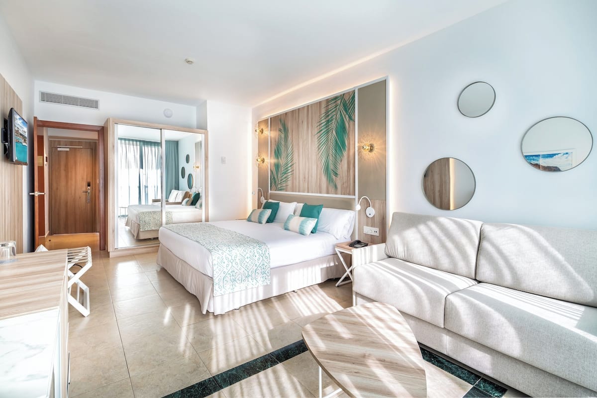 Une chambre d’hôtel moderne avec un grand lit, un canapé, une petite table et un téléviseur.