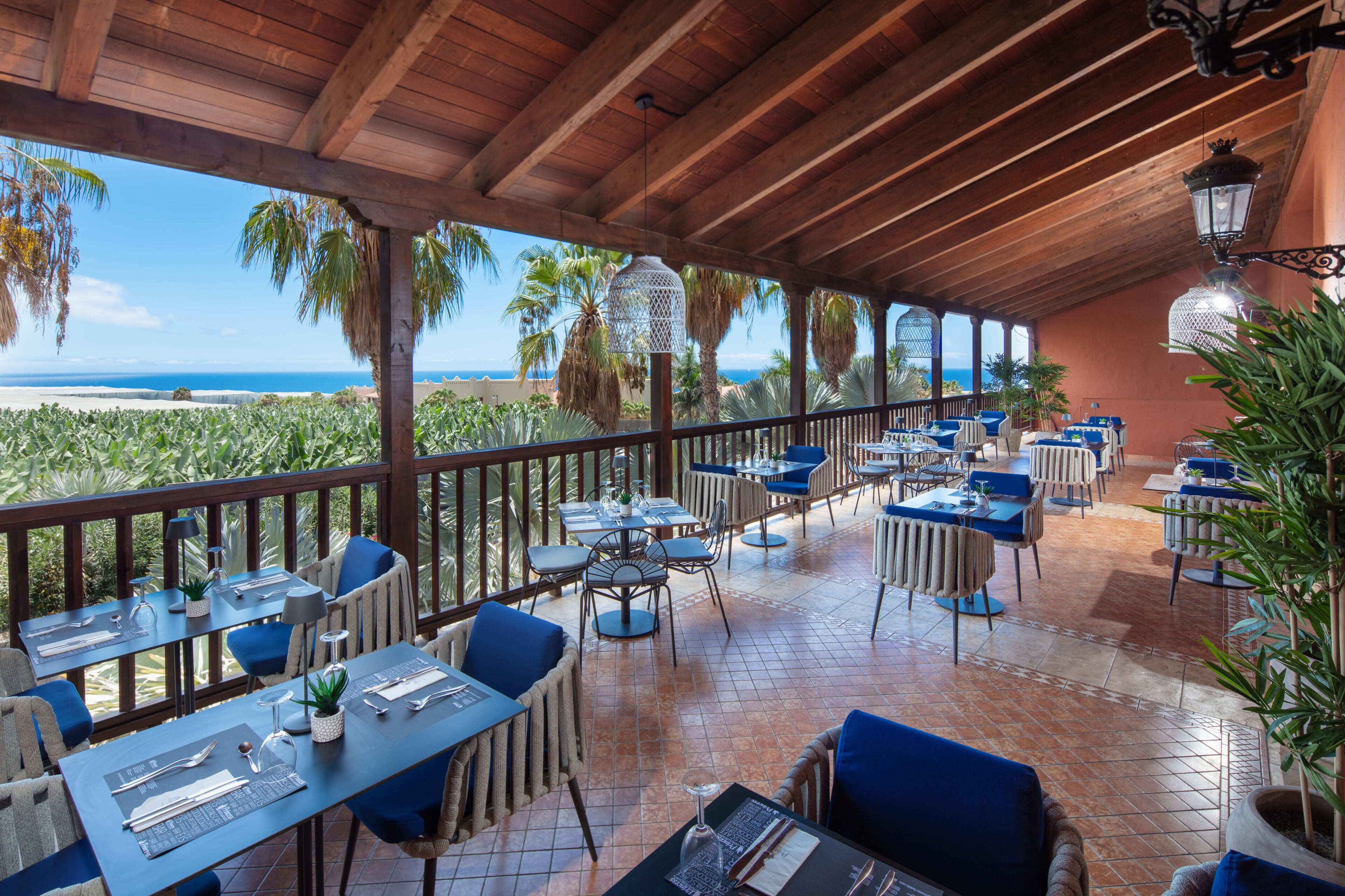 A covered outdoor dining area with tables and chairs, overlooking a beach.