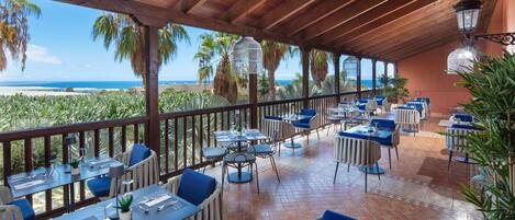A covered outdoor dining area with tables and chairs, overlooking a beach.