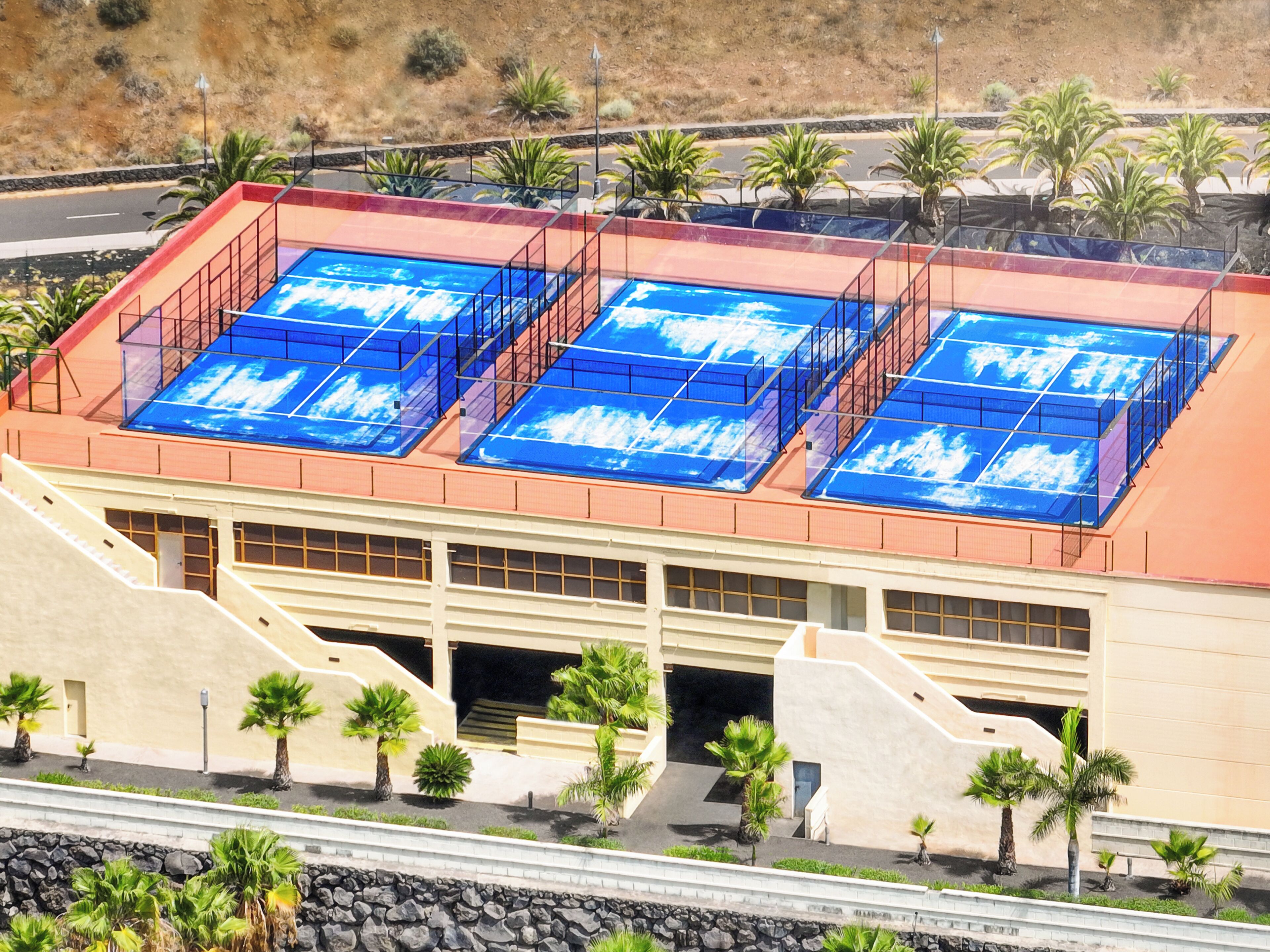 Un edificio de techo plano, con varias ventanas y un estacionamiento con palmeras.