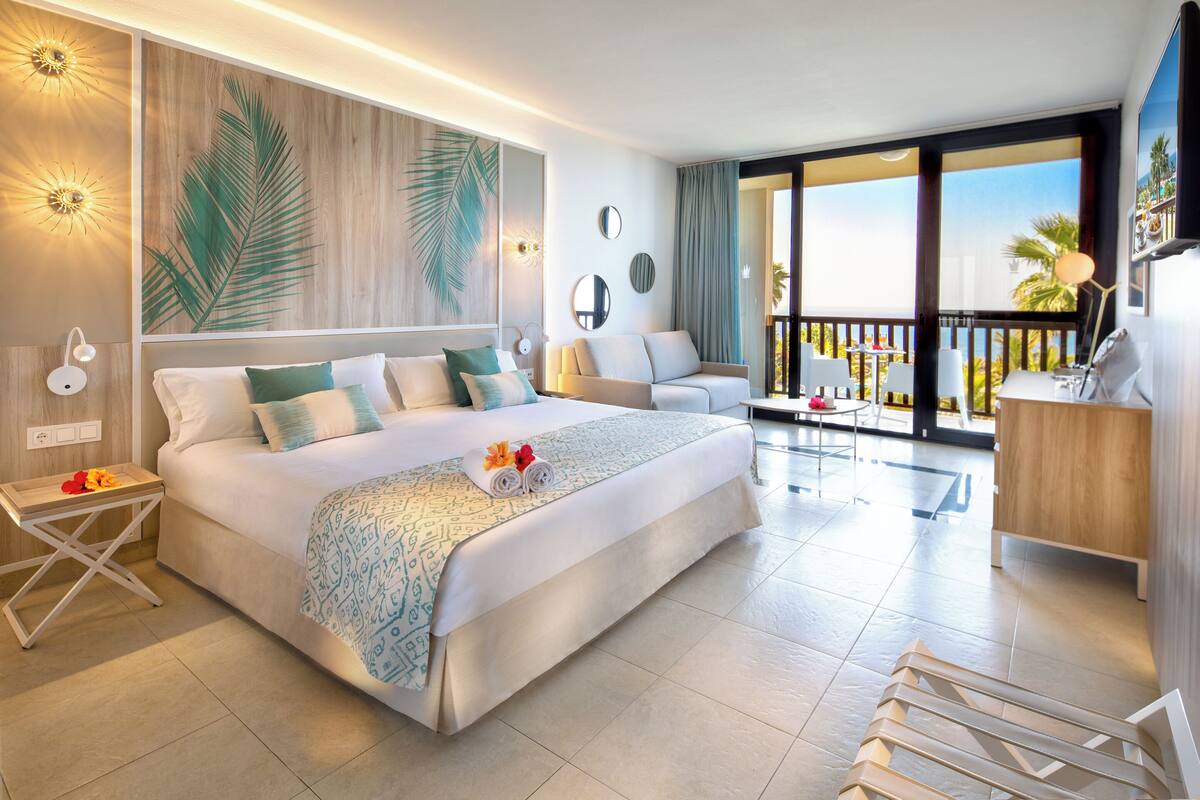 Une chambre d’hôtel moderne dotée d’un grand lit, d’un balcon avec vue, d’un coin salon et d’un bureau.