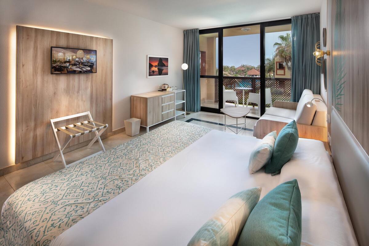 Une chambre d’hôtel moderne, dotée d’un grand lit, d’un bureau, d’une chaise et offrant une vue sur l’extérieur.