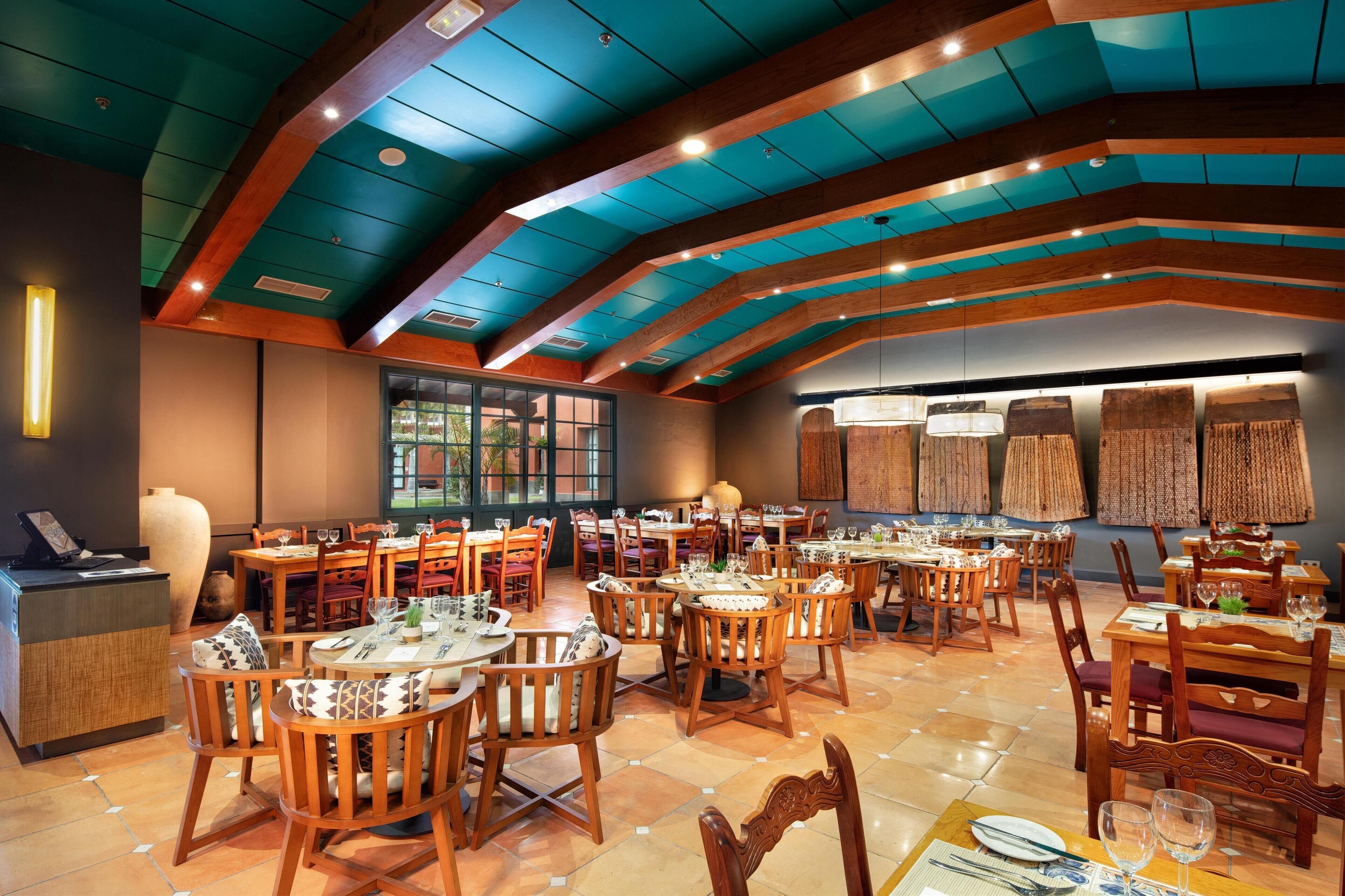 Un restaurant avec des tables et des chaises en bois, un comptoir d’accueil et un grand vase.