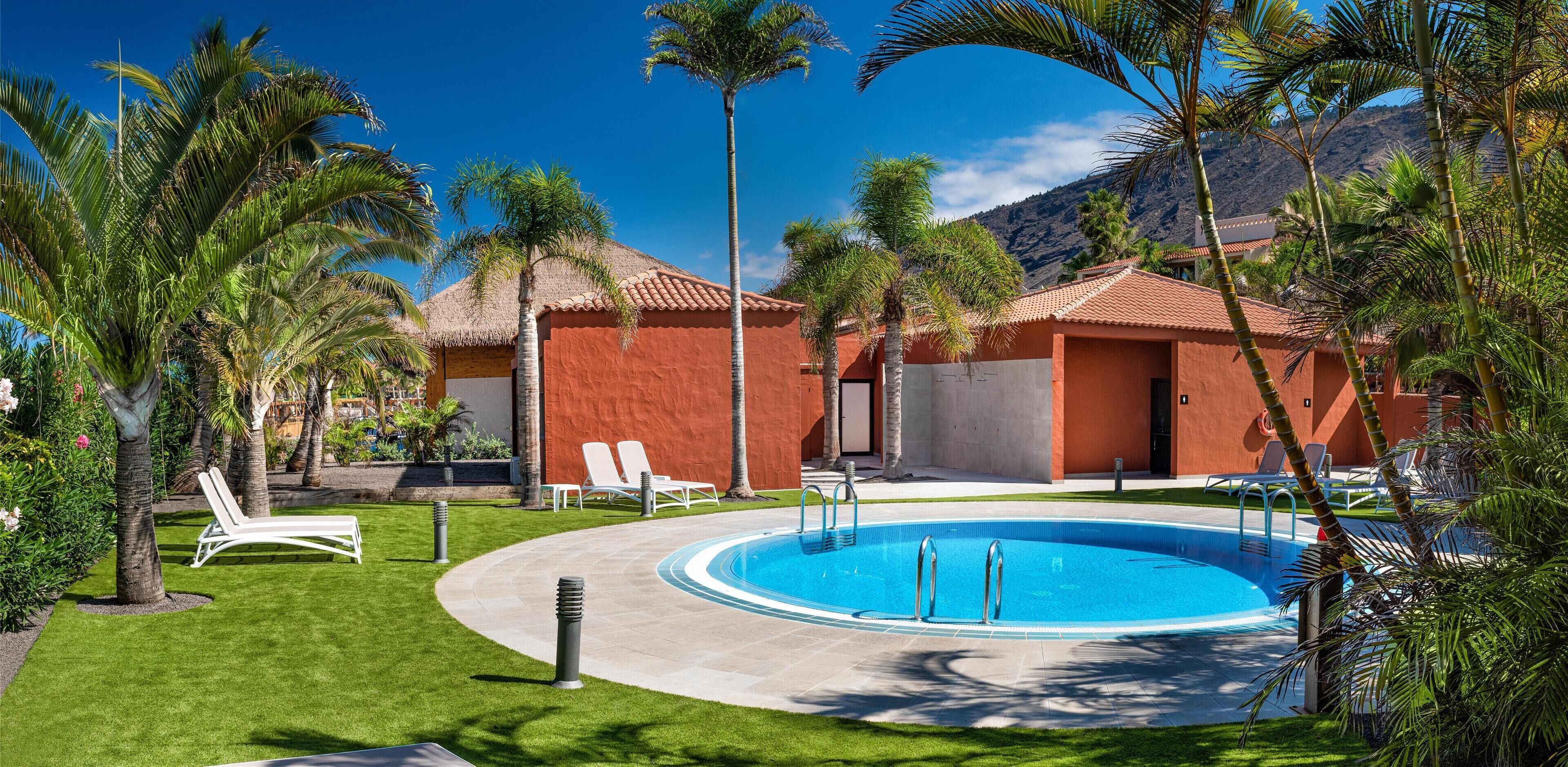 Un espace piscine avec une eau d’un bleu limpide, des chaises longues blanches et des palmiers.