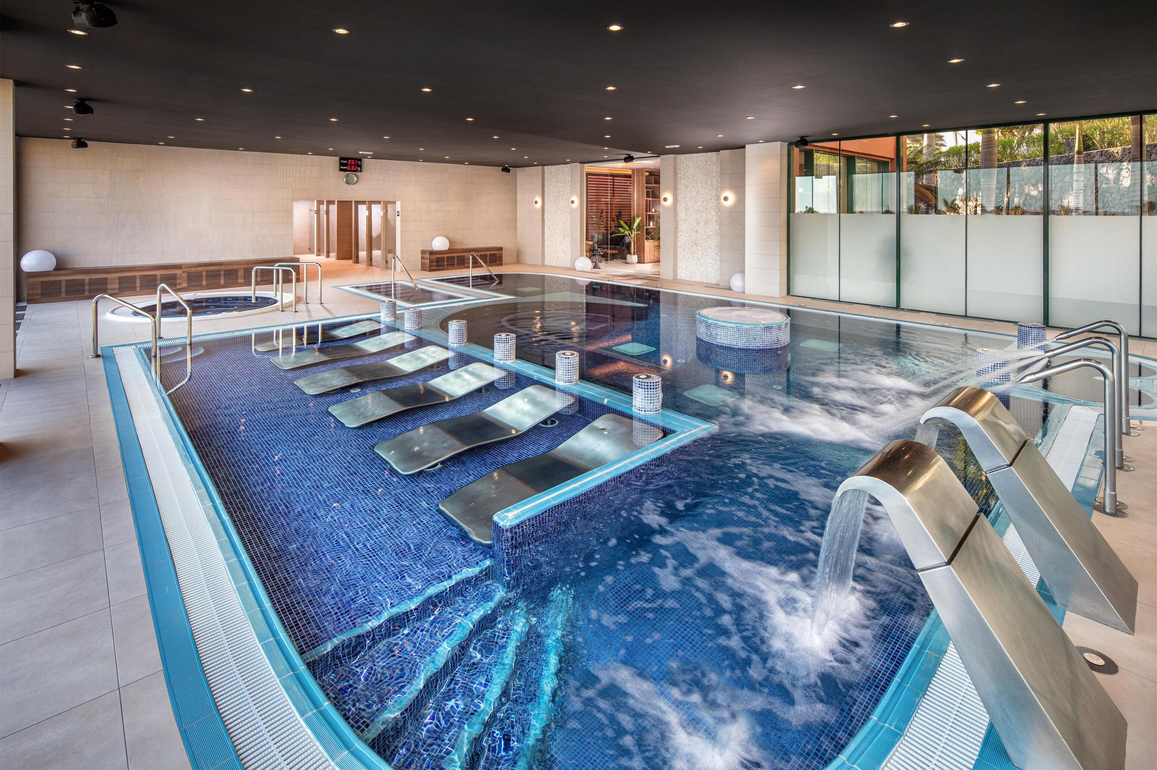 A large indoor swimming pool with multiple lanes, a water slide, and a sauna area.