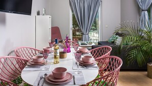 A dining area with pink chairs, a white table set with pink bowls and wine glasses, and a view of a balcony with curtains. - Thea Artemis (Chania)