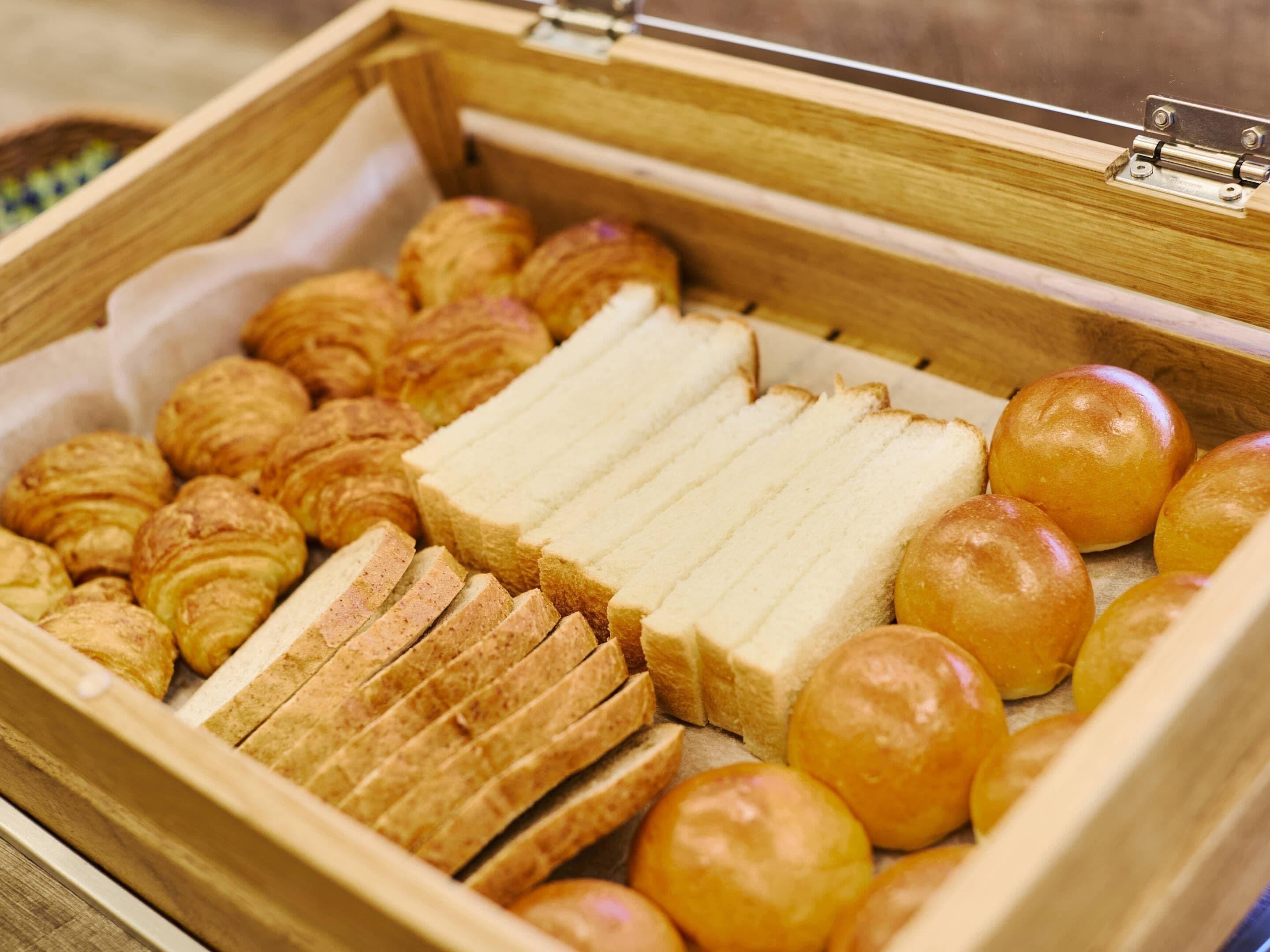 A wooden bread basket with various types of bread and pastries.