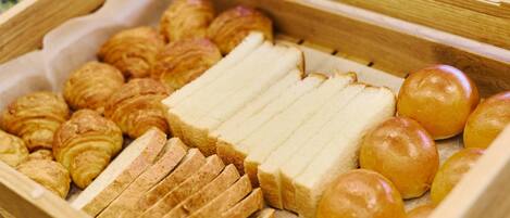 A wooden bread basket with various types of bread and pastries.