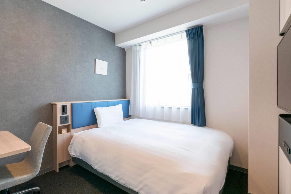 Une chambre d’hôtel équipée d’un lit, d’un bureau, d’une chaise, d’une télévision et d’une fenêtre avec des rideaux.