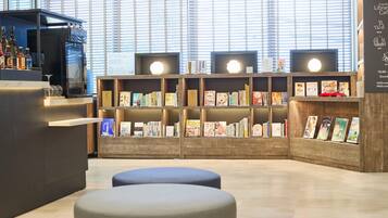 A library with bookshelves, seating areas, and a counter with beverages.