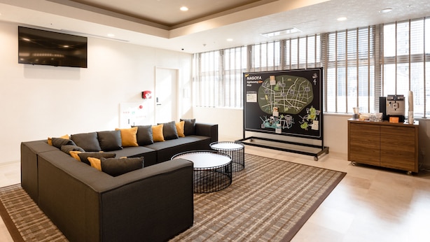 A modern office space with a sectional sofa, a map display, and a coffee station. - Comfort Hotel ERA Nagoya Meiekiminami (Nagoya)