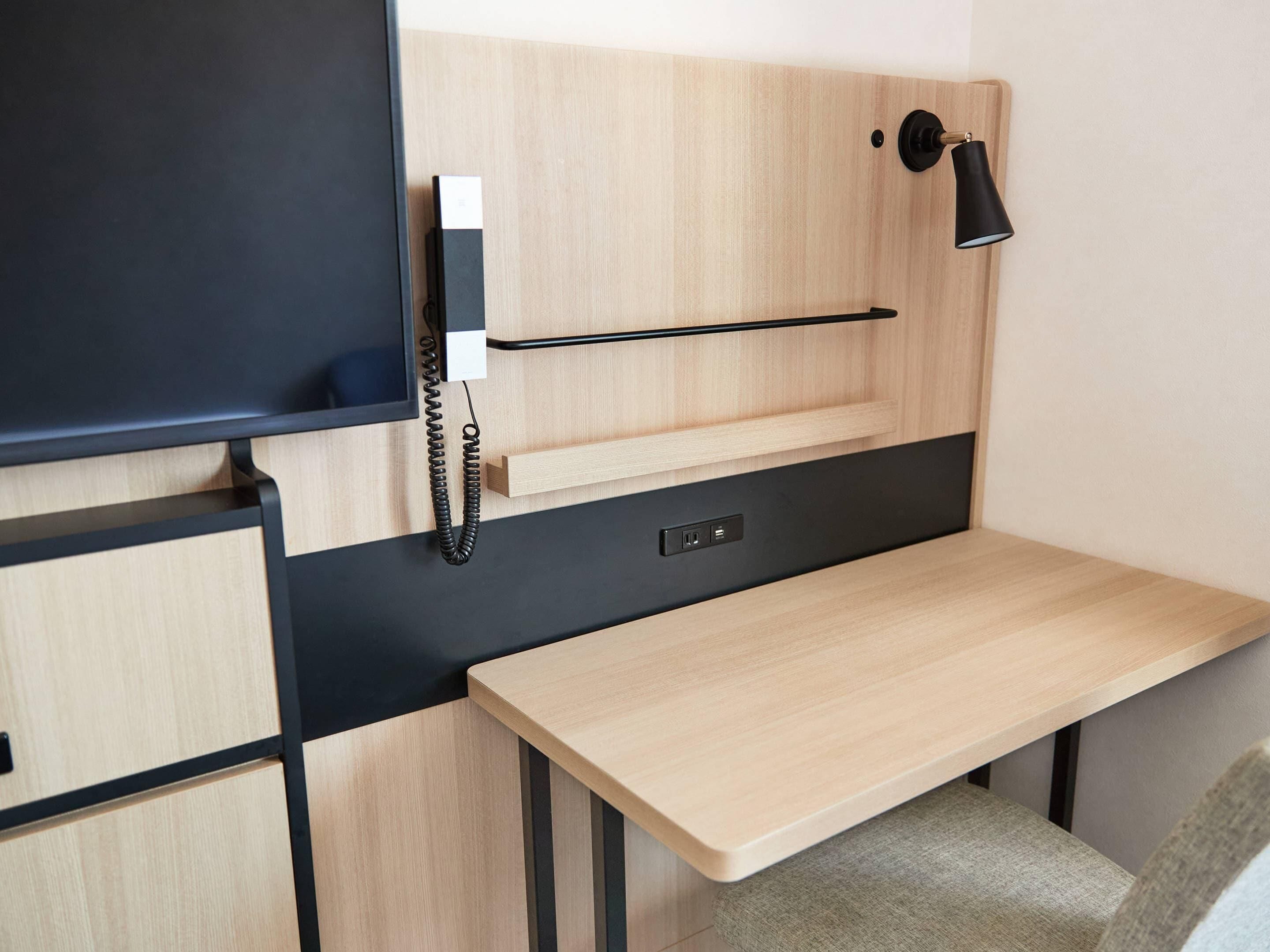 A compact room with a desk, a mounted telephone, and a wall-mounted lamp.