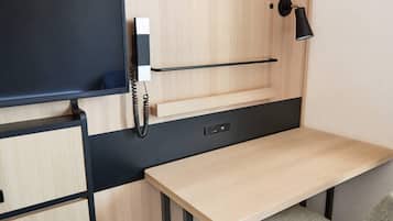 A compact room with a desk, a mounted telephone, and a wall-mounted lamp.