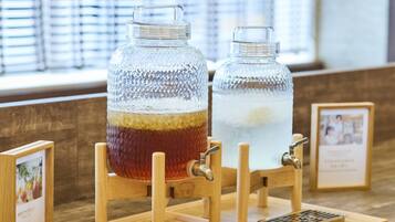 Two glass jars on wooden stands with taps, likely for serving beverages, on a wooden table with a window in the background.